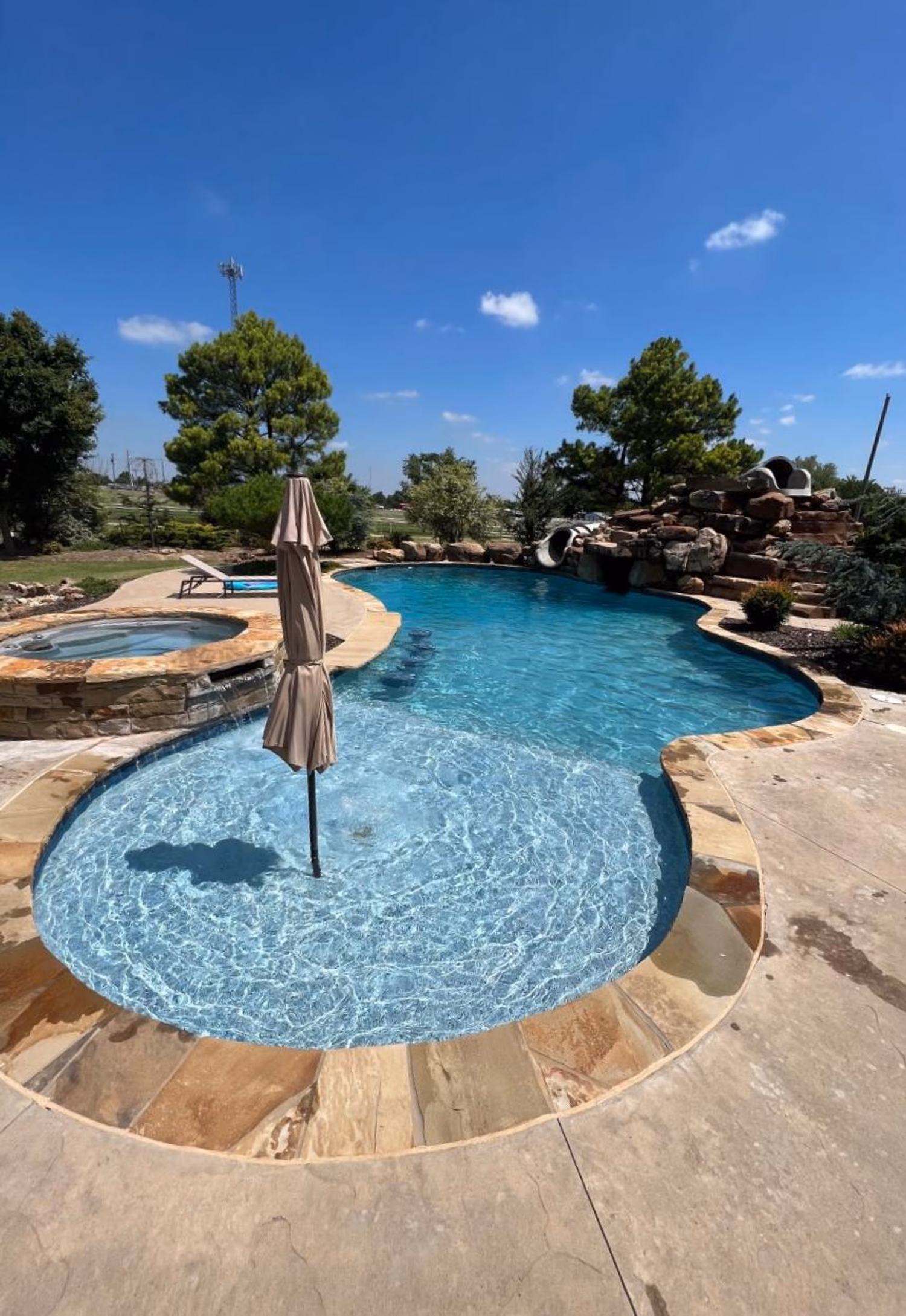 Freeform pool with stone waterfall and spa under blue sky